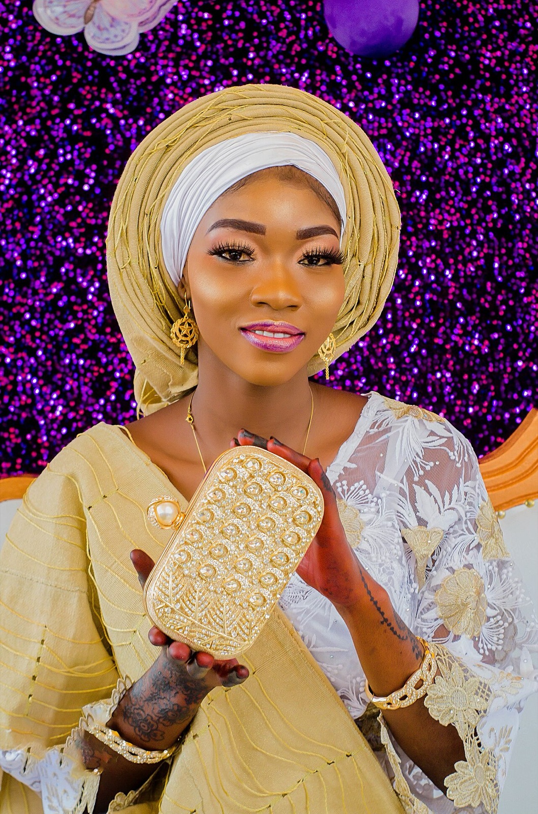 Woman in gold gele and lace holding a beaded clutch