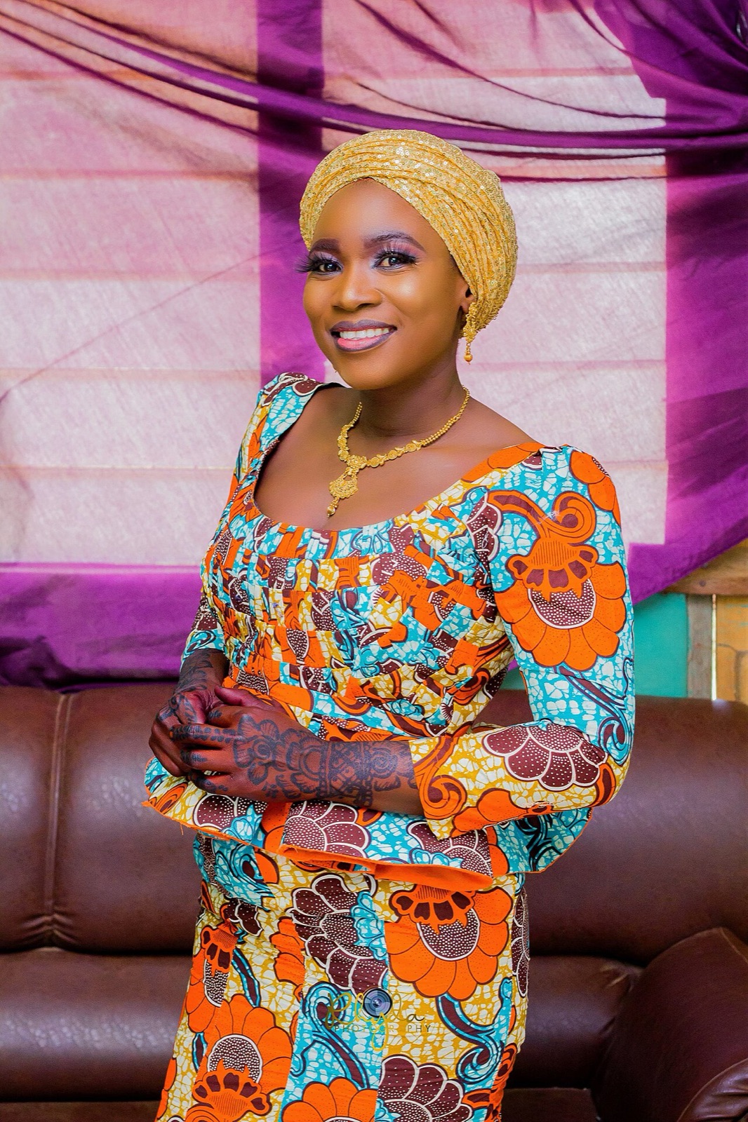 Woman in an orange and teal print dress and gold headwrap