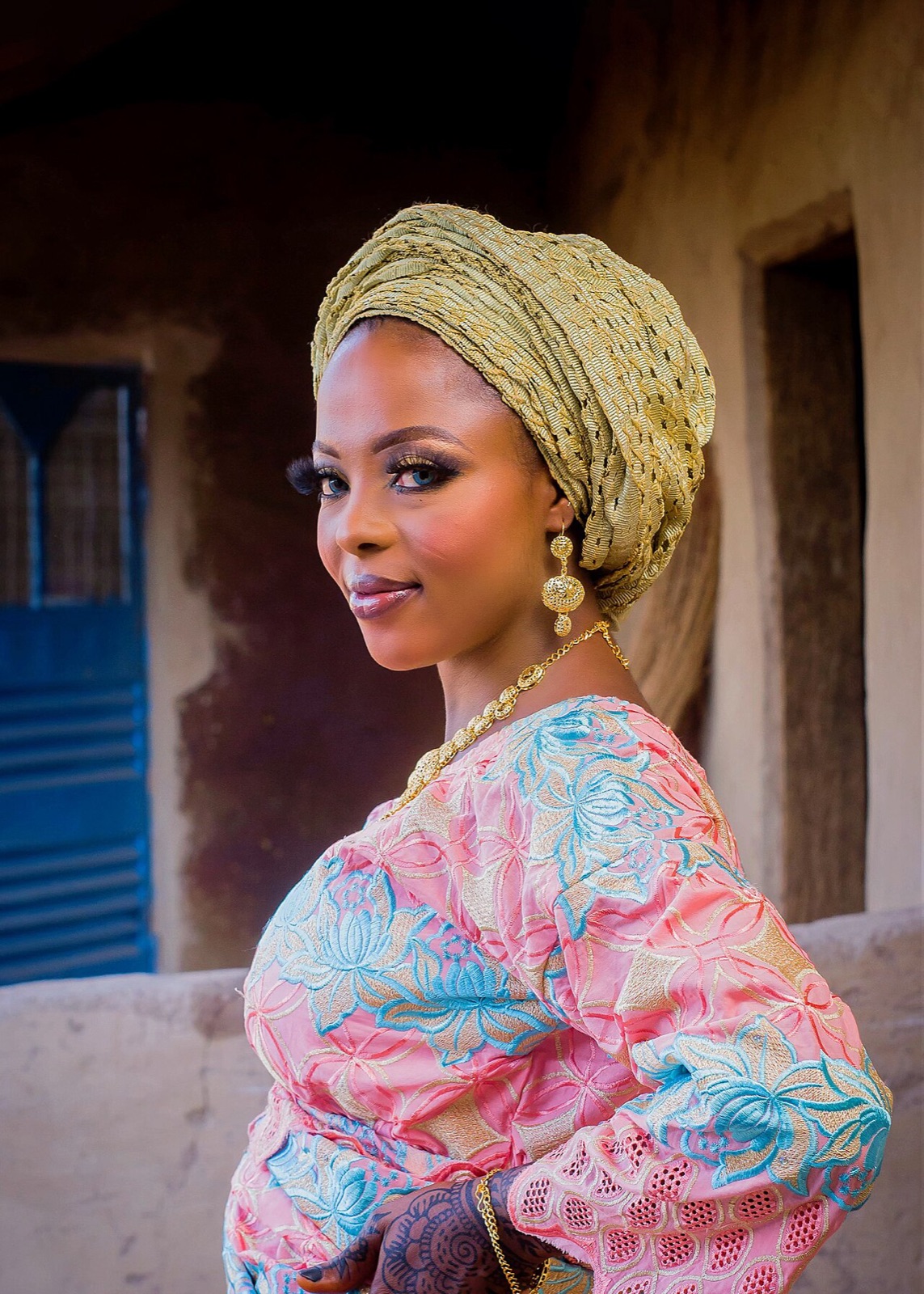 Woman in a gold headwrap and floral dress standing in a doorway